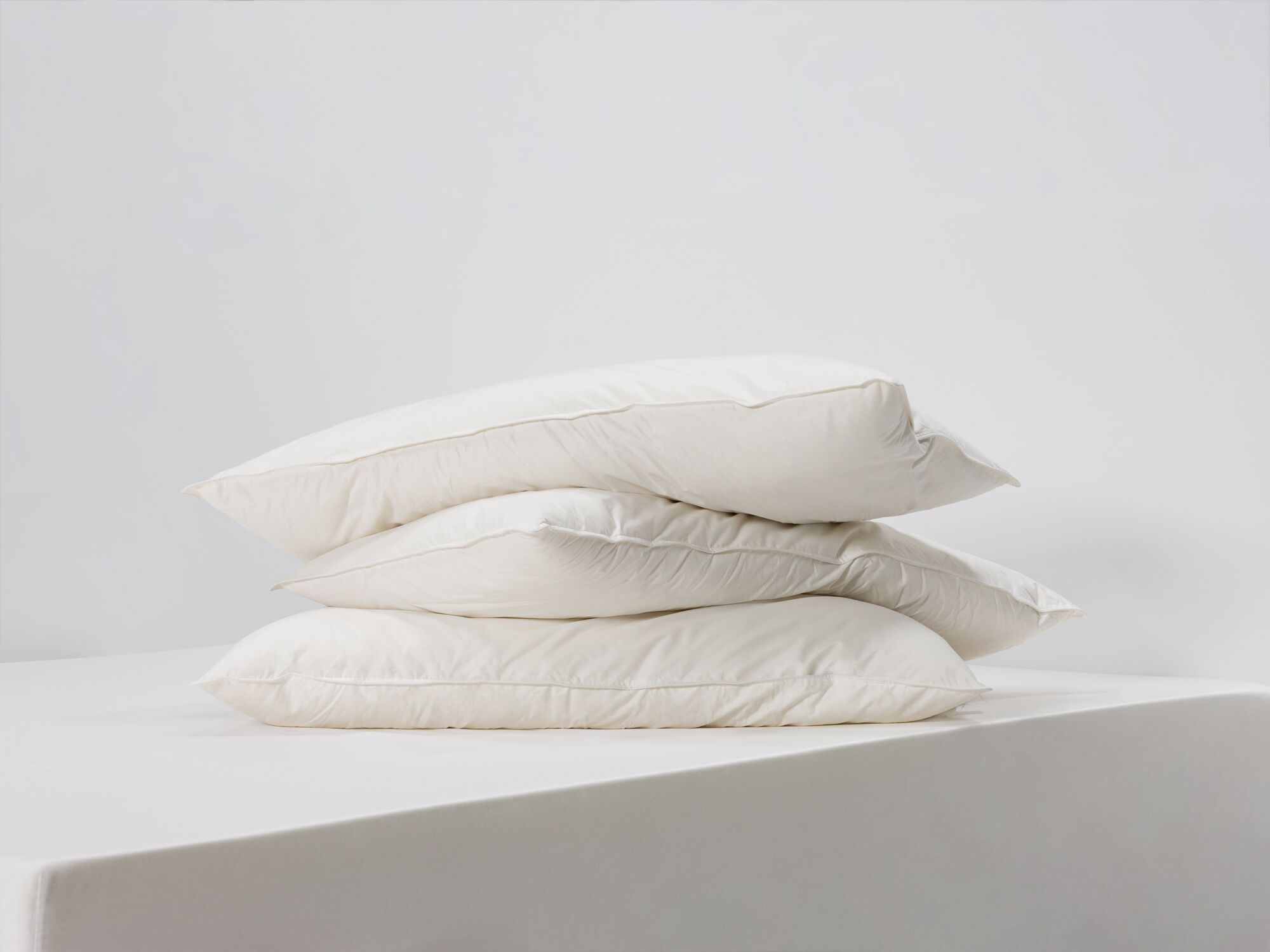 Three king size feather pillows stacked side angle view